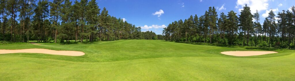 Golf course fairway framed by pine trees and sand bunkers under a blue sky