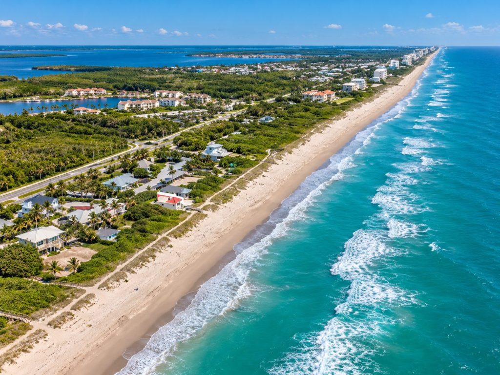 Aerial view of the Treasure Coast shoreline with beachfront homes, a lagoon inlet, and turquoise Atlantic surf